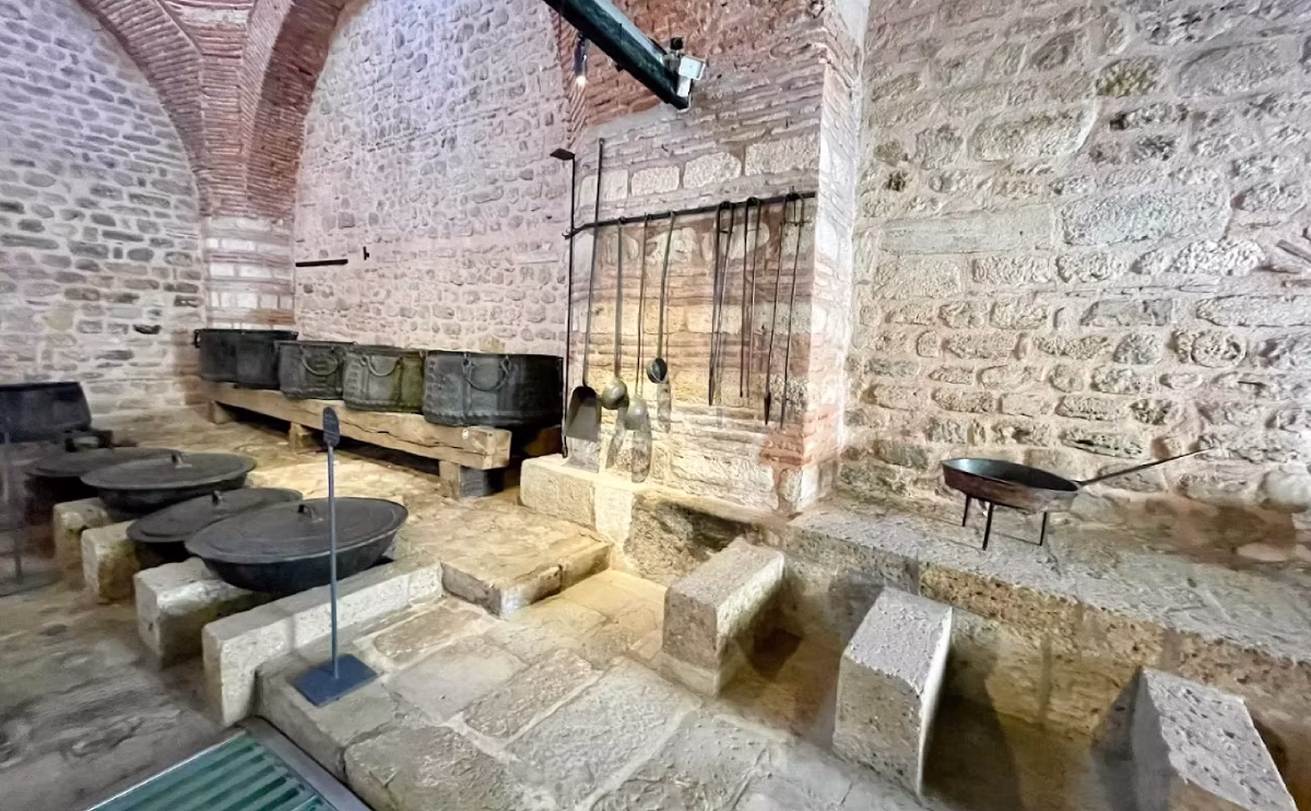 Historic Ottoman kitchen with large cauldrons and stone hearth inside Topkapi Palace kitchens.